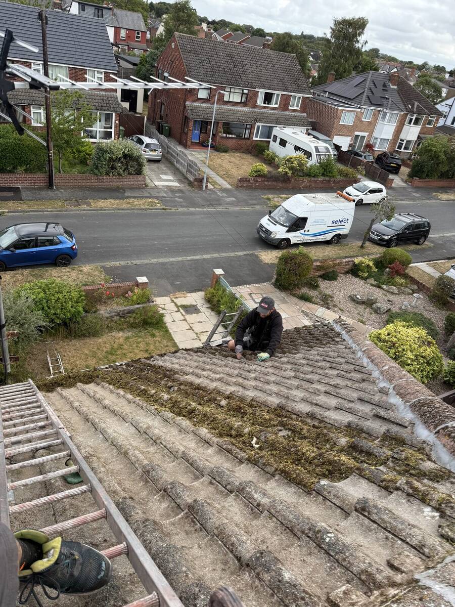 Roofer hand-clearing moss near a chimney stack in Crosby